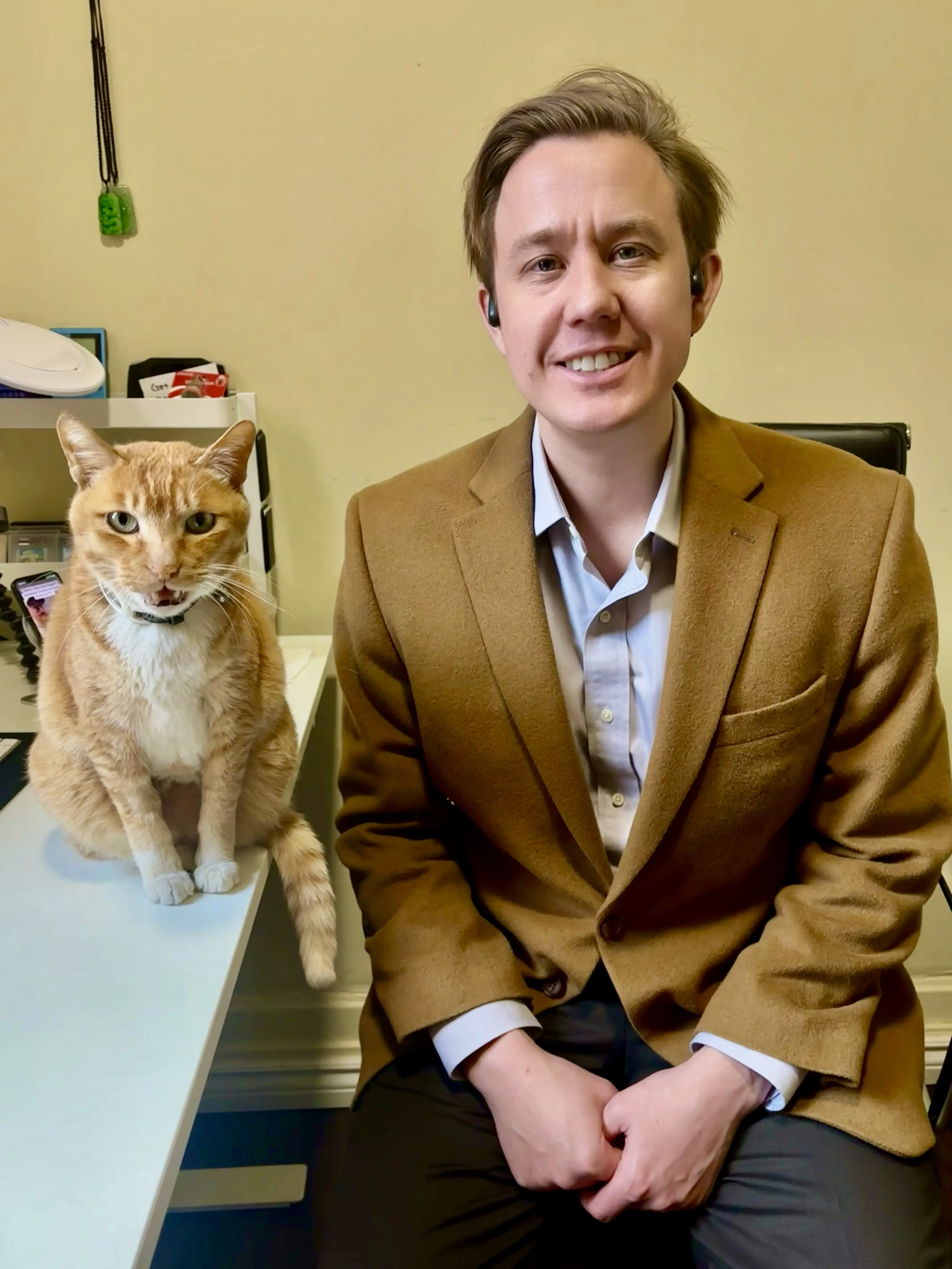 Ian Heraty sits beside Turkey, an orange tabby cat, in an office. Ian is smiling at the camera while Turkey appears to be meowing. They are the co-founders of Receipt AI.