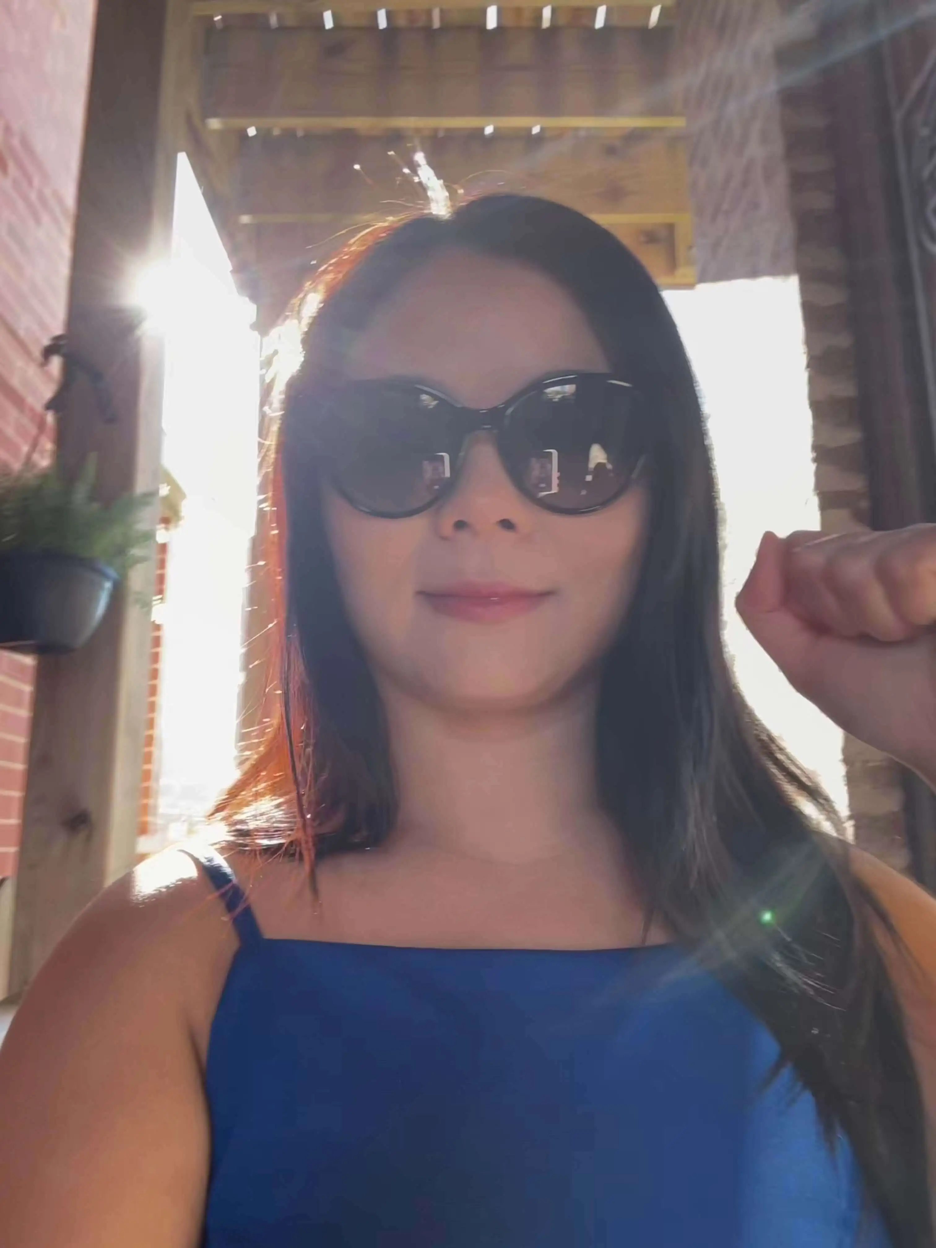 Founder of Receipt-AI.com Queenie Peng in sunglasses standing in sunlight with her fist raised, symbolizing determination and resilience while building a company - the hardest thing she has ever done.